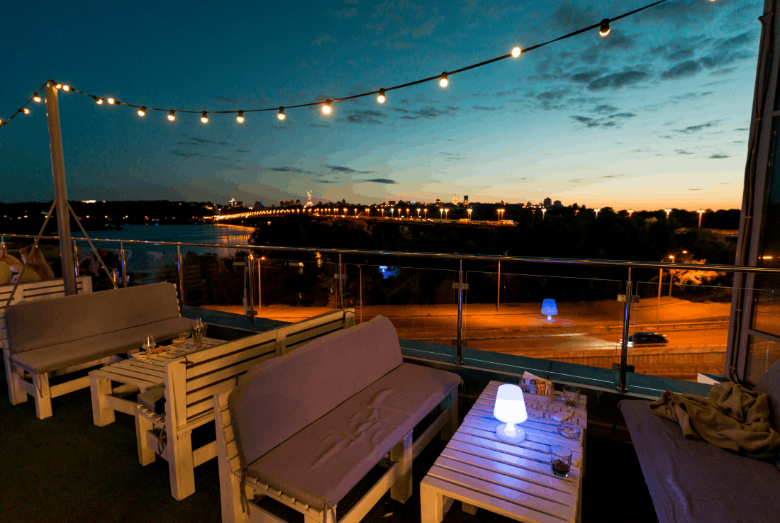 Panoramic rooftop dining area with string lights and city skyline view